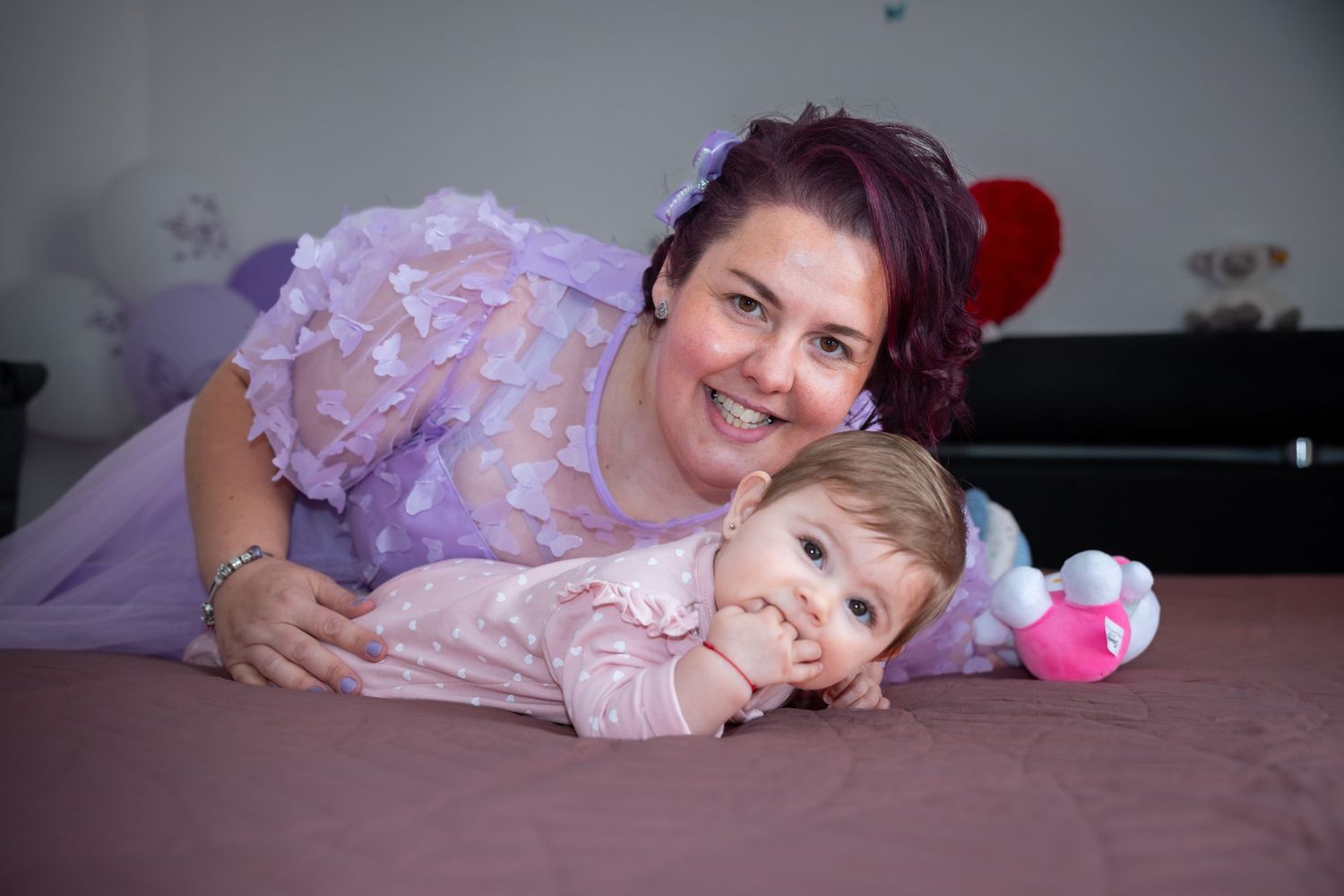 Karoline liegt neben ihrer lächelnden Mutter auf dem Bett zu Hause.
