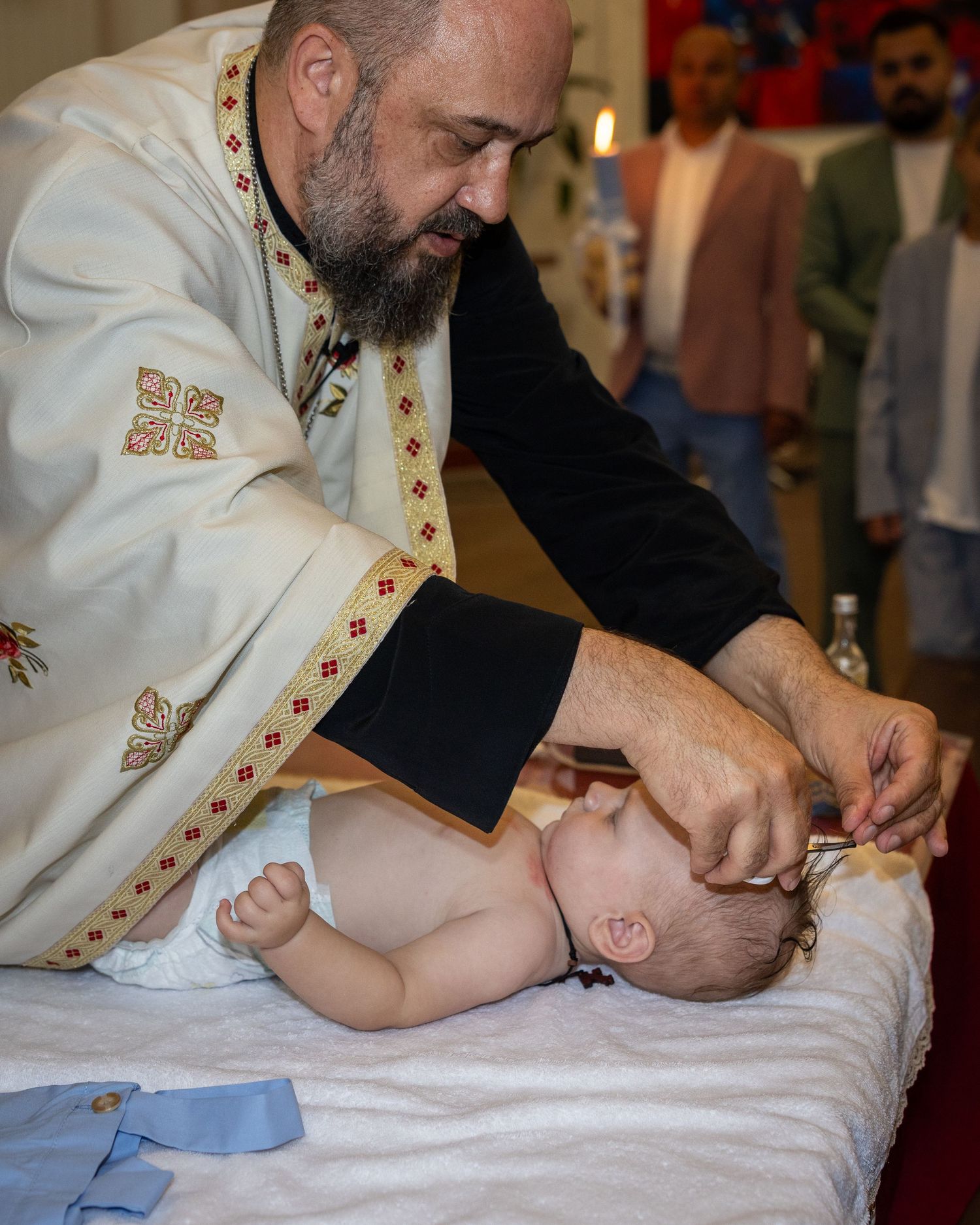 Der Priester hält eine Haarsträhne von Aris zwischen den Fingern und setzt eine kleine Schere an.