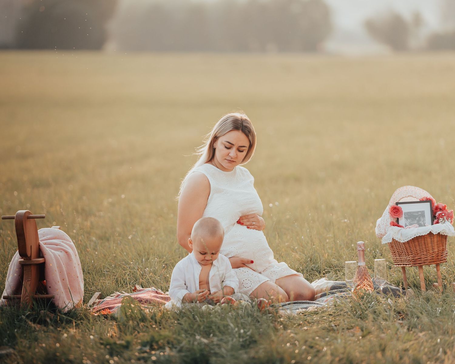 Mother and baby enjoying a sunny outdoor picnic on a blanket in a green meadow field.