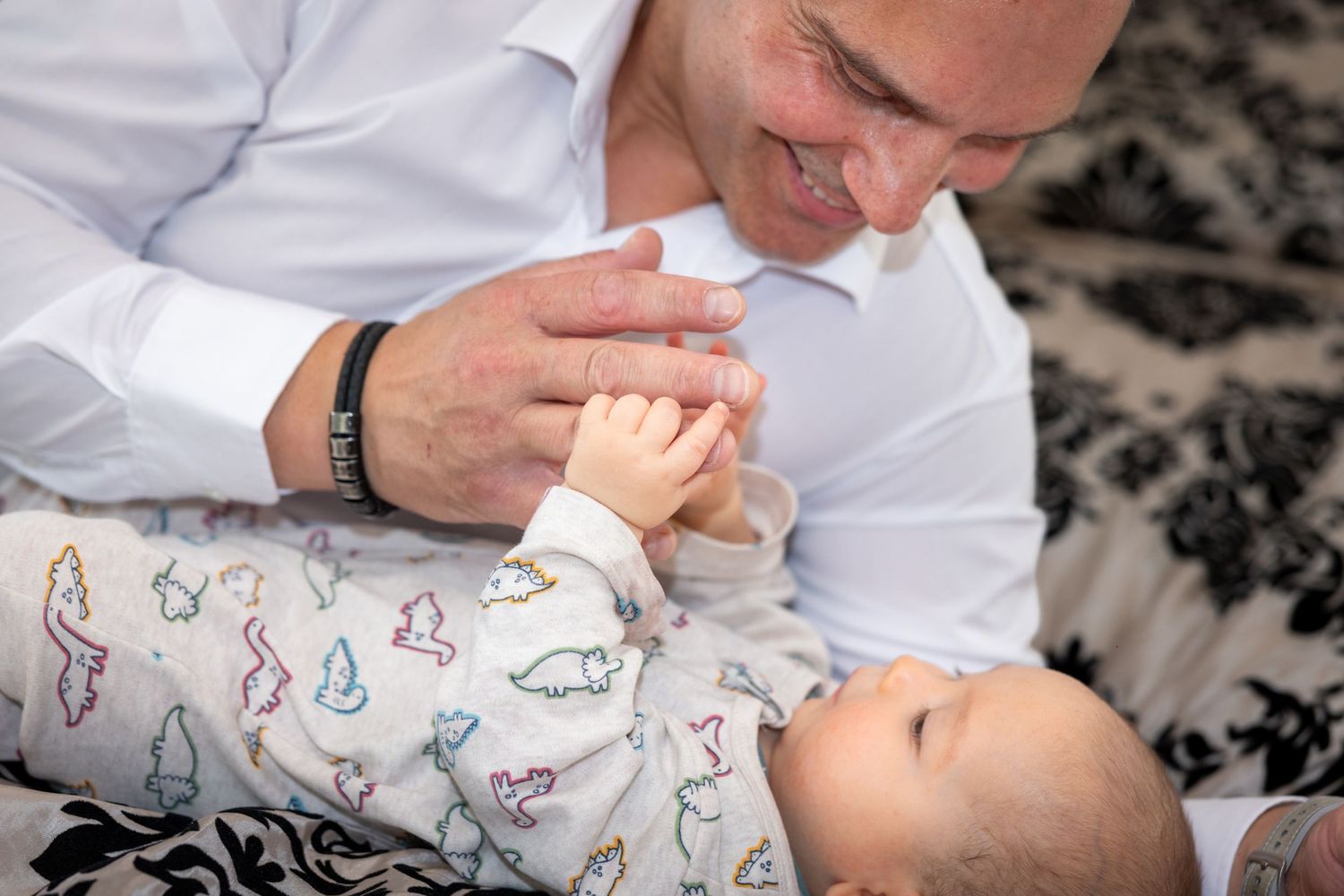 Milans Vater küsst seine Hand, während er auf einer gemusterten Decke liegt.