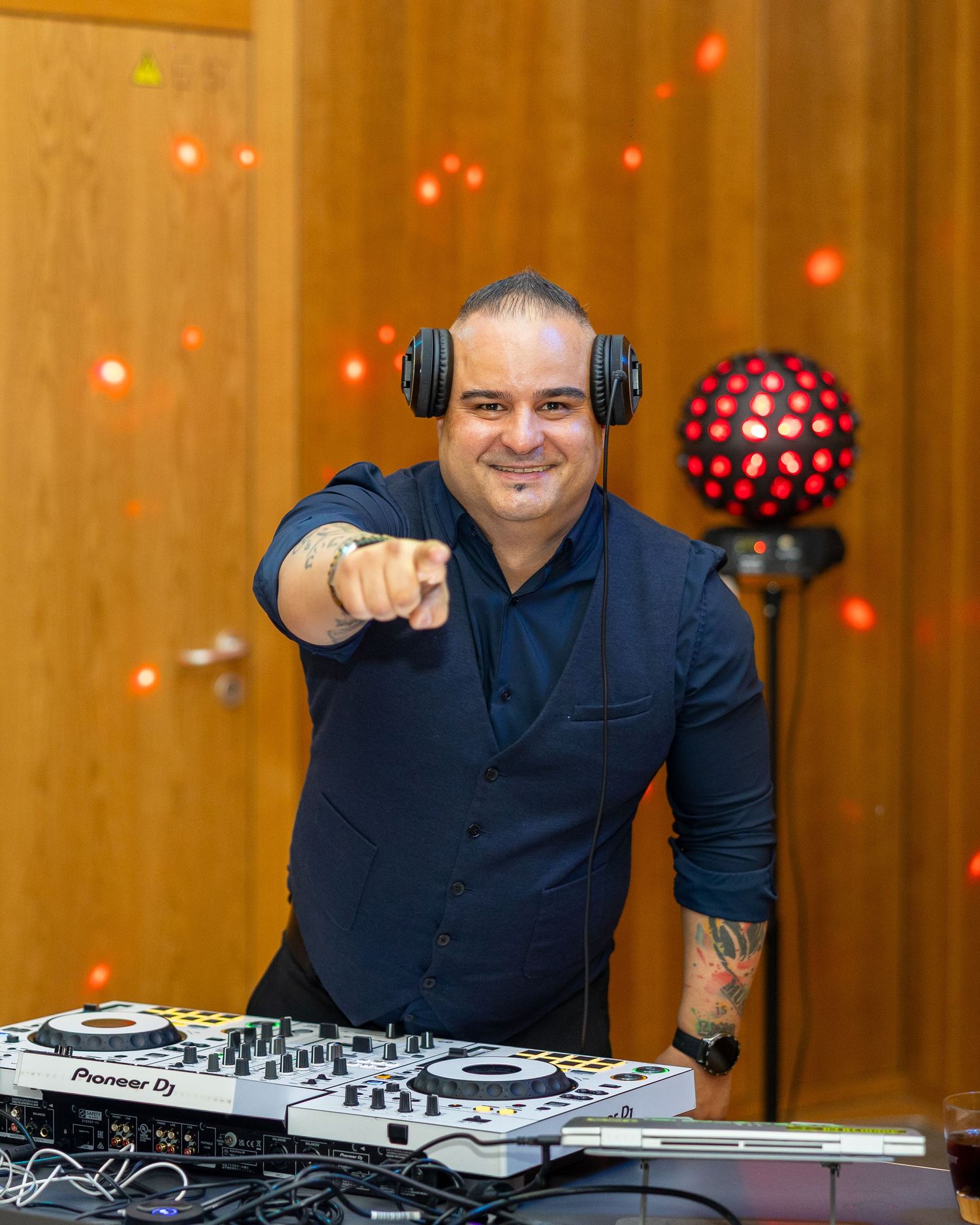 Der DJ steht mit Kopfhörern hinter seinem Mischpult und zeigt in die Kamera.