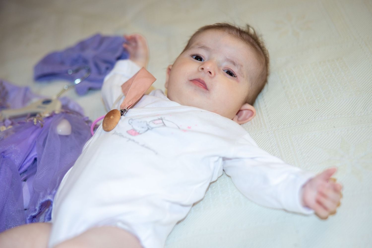 Alexia Ioana liegt in weißer Kleidung auf einer hellen Decke; neben ihr liegt ein violettes Kleid.