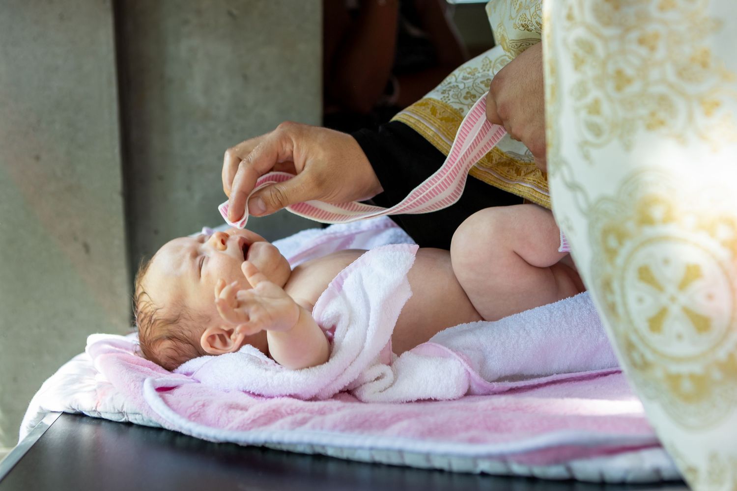 Priest administering communion to a newborn baby during a Christian baptism ceremony.