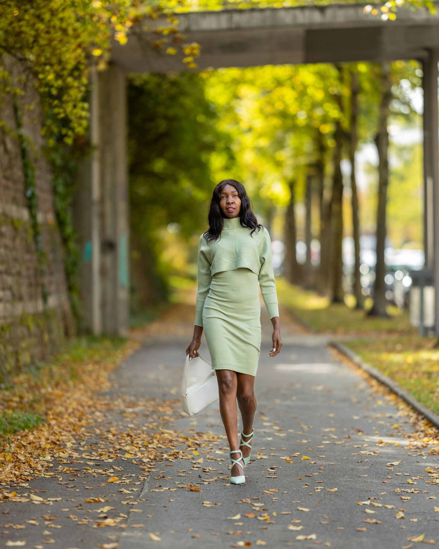 Jacky geht im hellgrünen Kleid durch eine von Herbstlaub gerahmte Allee