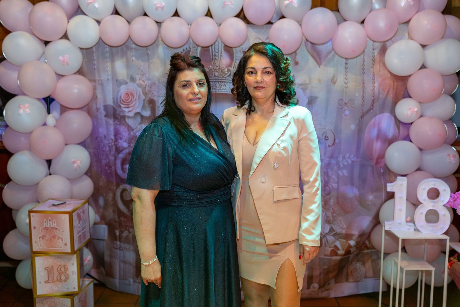 Zwei Frauen stehen vor rosafarbenen Luftballons und der leuchtenden Zahl 18.