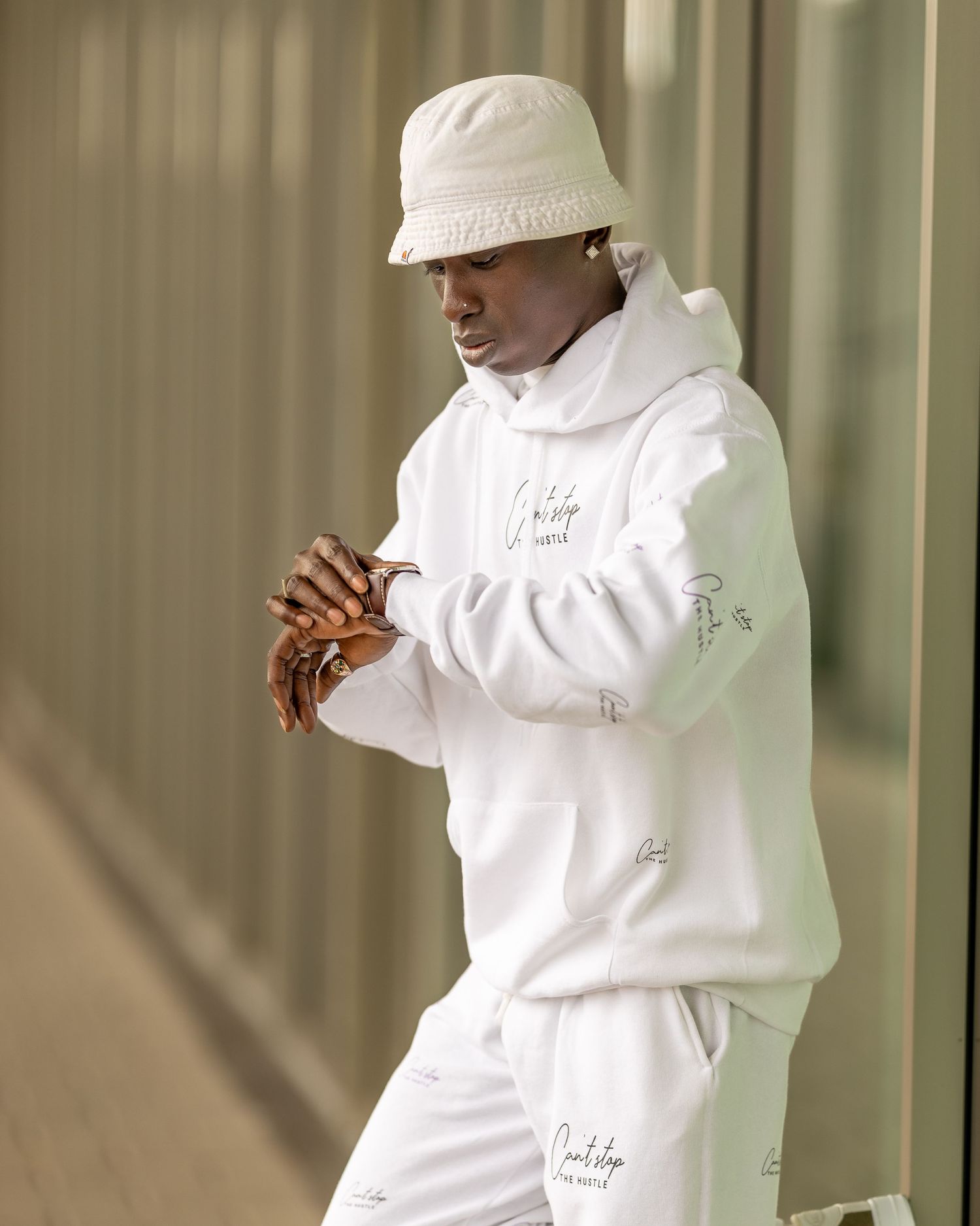 Young man wearing a matching all-white hoodie and pants with a white bucket hat, posing outdoors.