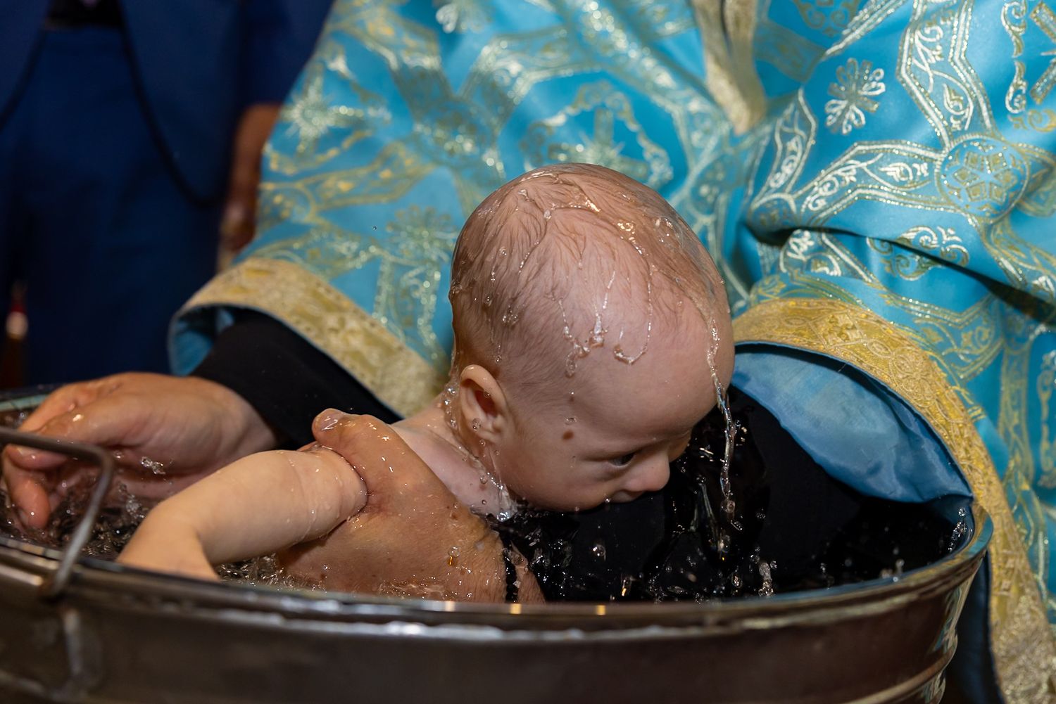 Baby being baptized in a traditional Orthodox Christian christening ceremony with water immersion in a baptismal font.