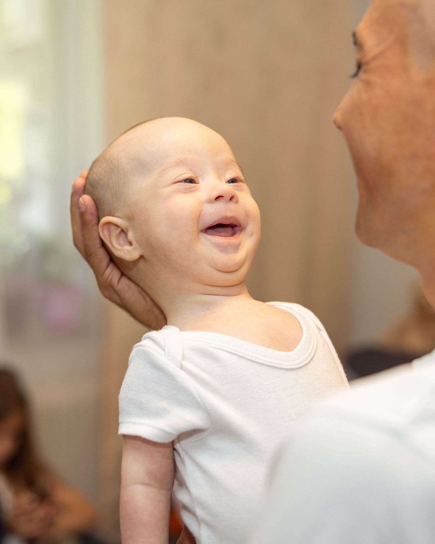 Ein lächelndes Baby wird in einem hellen Raum auf dem Arm gehalten.