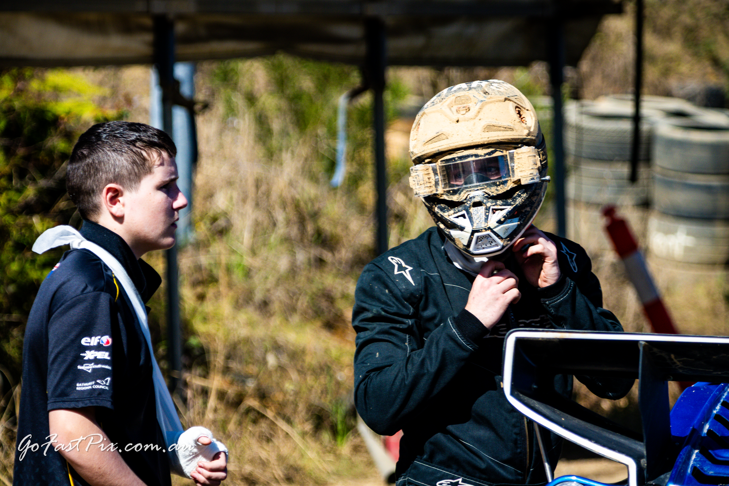 Racing driver adjusts helmet at outdoor karting or motorsport event.
