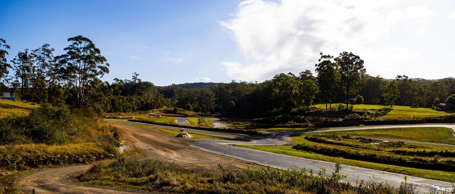 Panoramic view of winding motorsport circuit surrounded by lush green trees and hills.