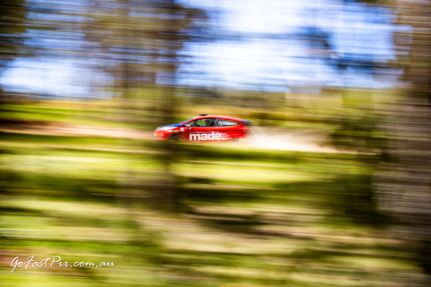 Motion blur action shot of a red Mazda rally car speeding through a green forest stage.