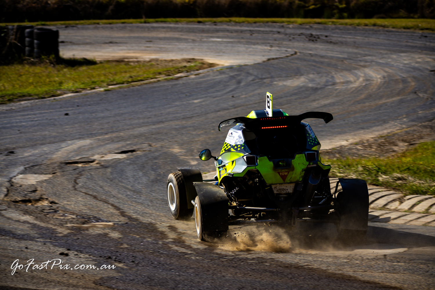 Green and black racing buggy cornering on a dirt track at speed.