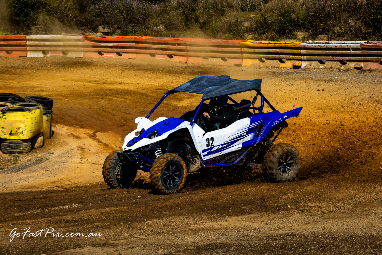 Blue and white off-road UTV racing through a dirt track kicking up dust.