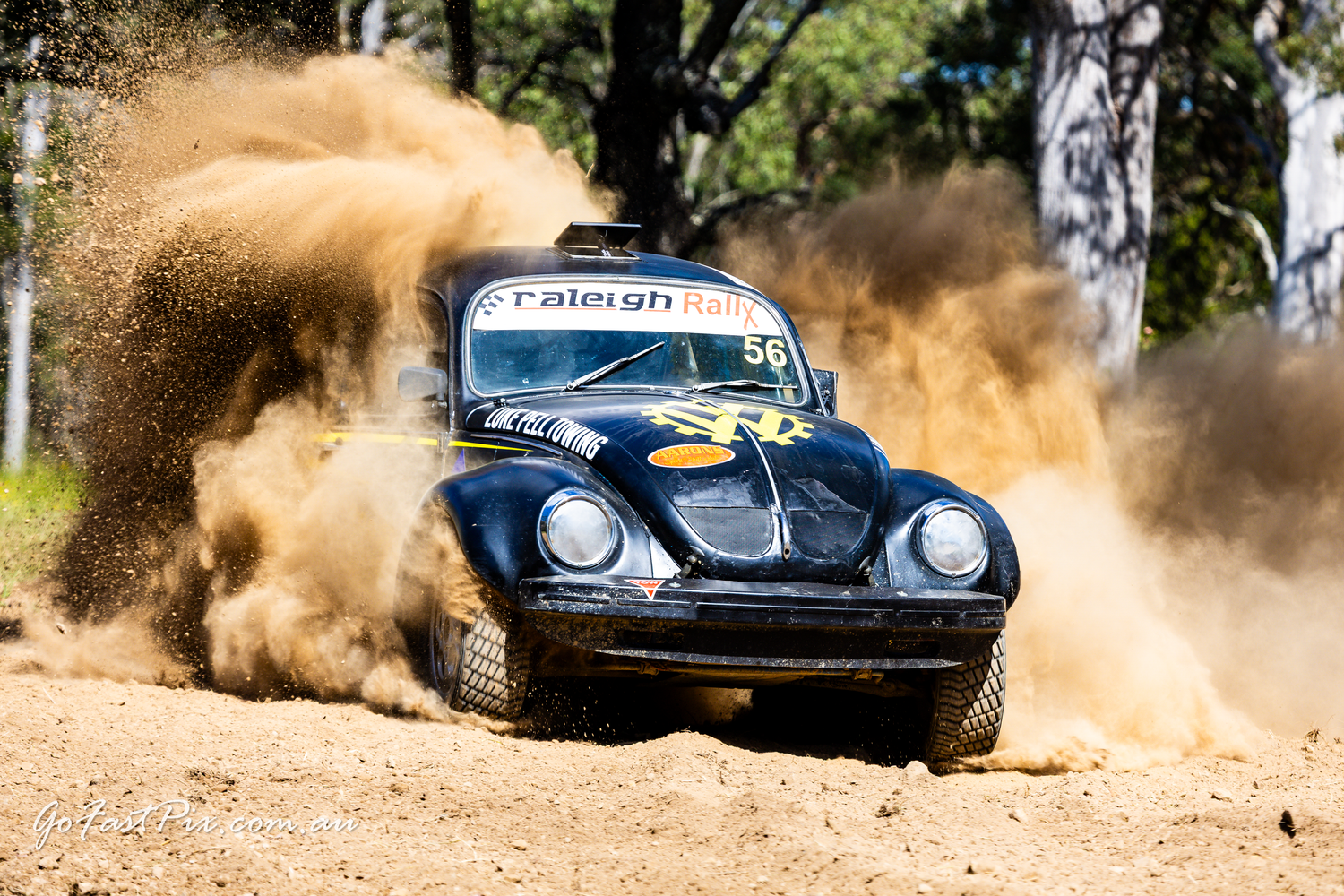 Black Volkswagen Beetle rally car kicking up dust on a dirt track during an off-road racing event.