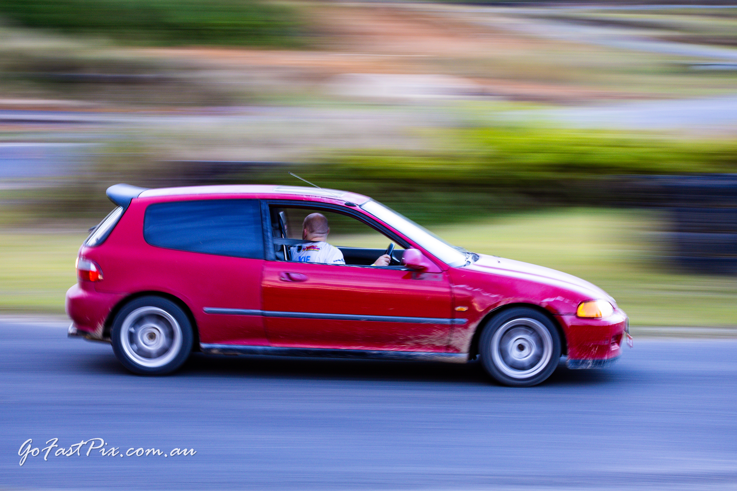 Red Honda Civic hatchback captured with motion blur on public road.