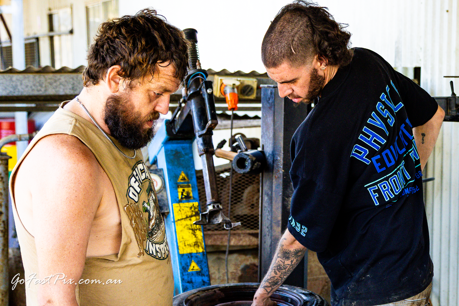 Two mechanics working on vehicle tyre in workshop at motorsport event.