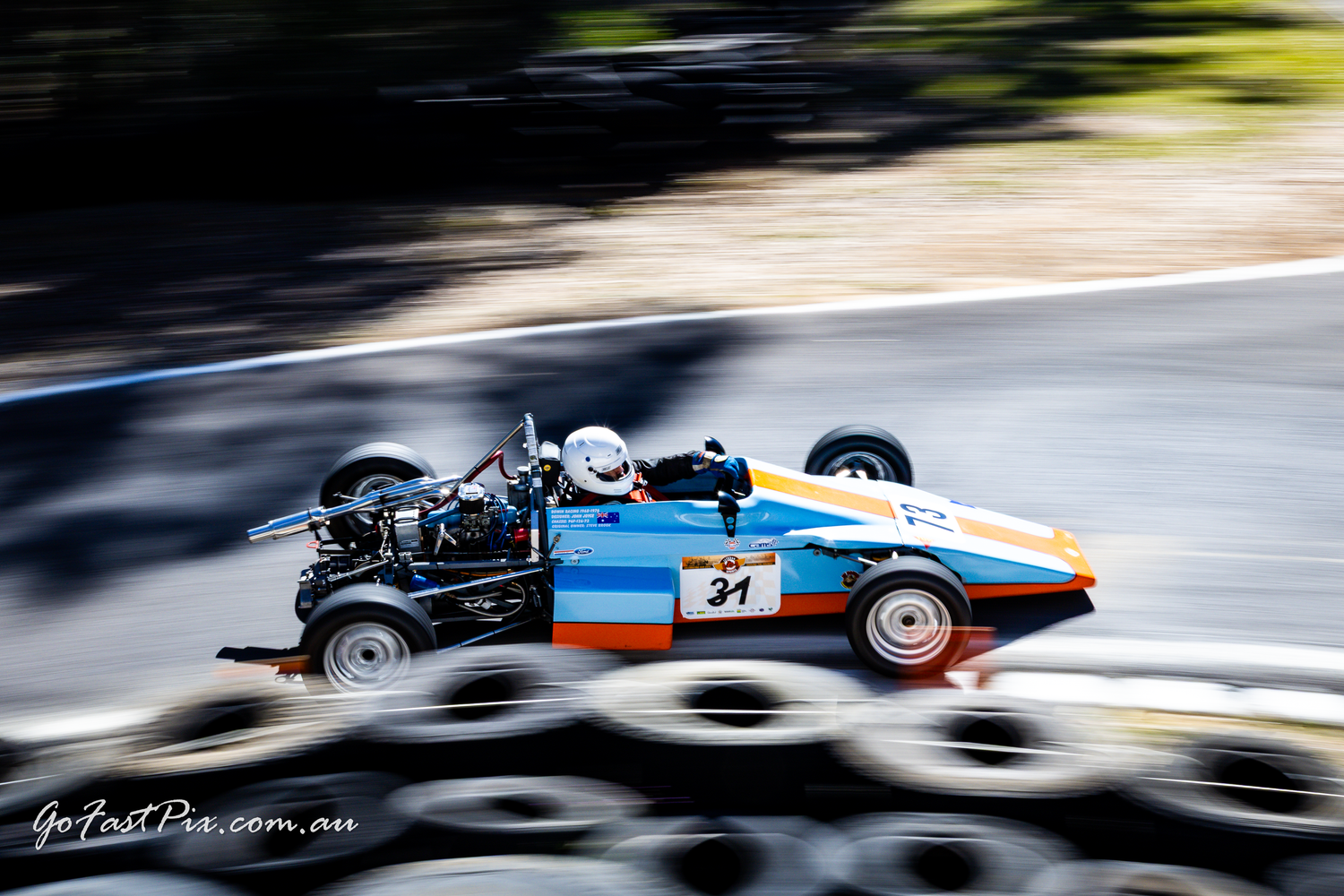 Blue vintage Formula Ford race car number 31 speeding past tire barriers.