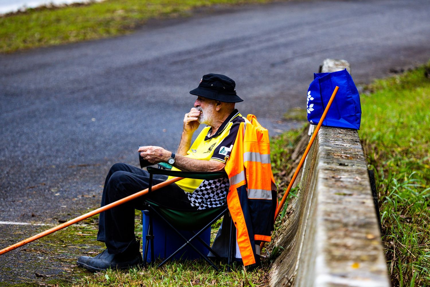 Race official in orange high-visibility vest sitting trackside monitoring wet weather motorsport event.