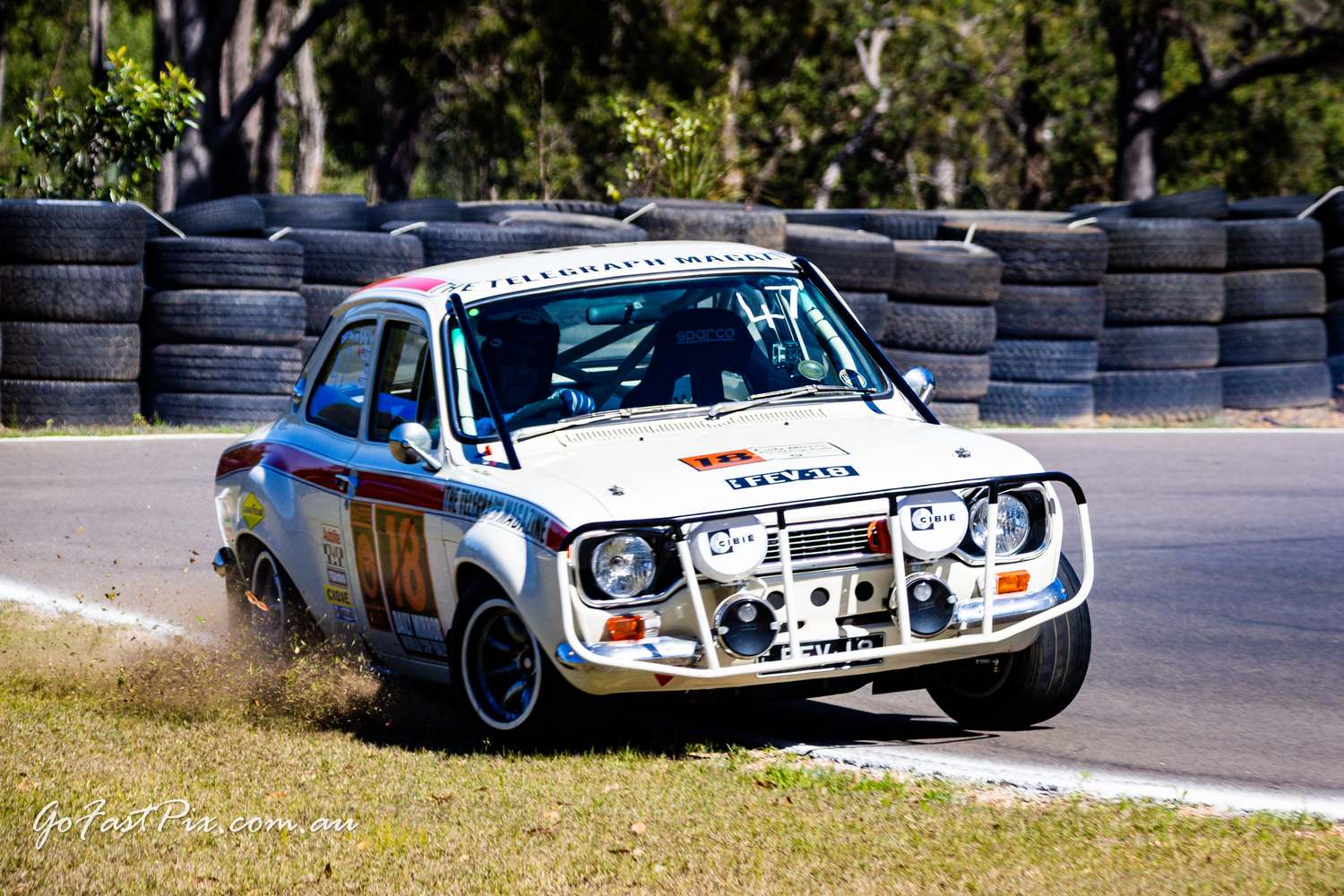 Classic Ford Escort rally car cornering on a circuit lined with tires.