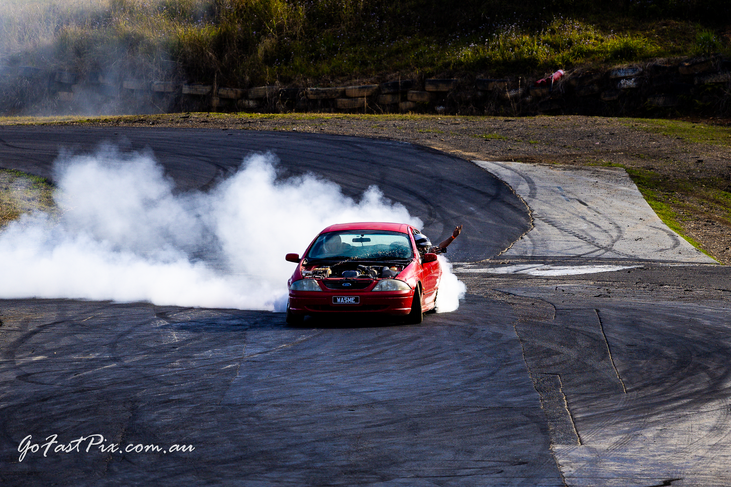 Red car drifting on a race track with large smoke clouds billowing from spinning tires.