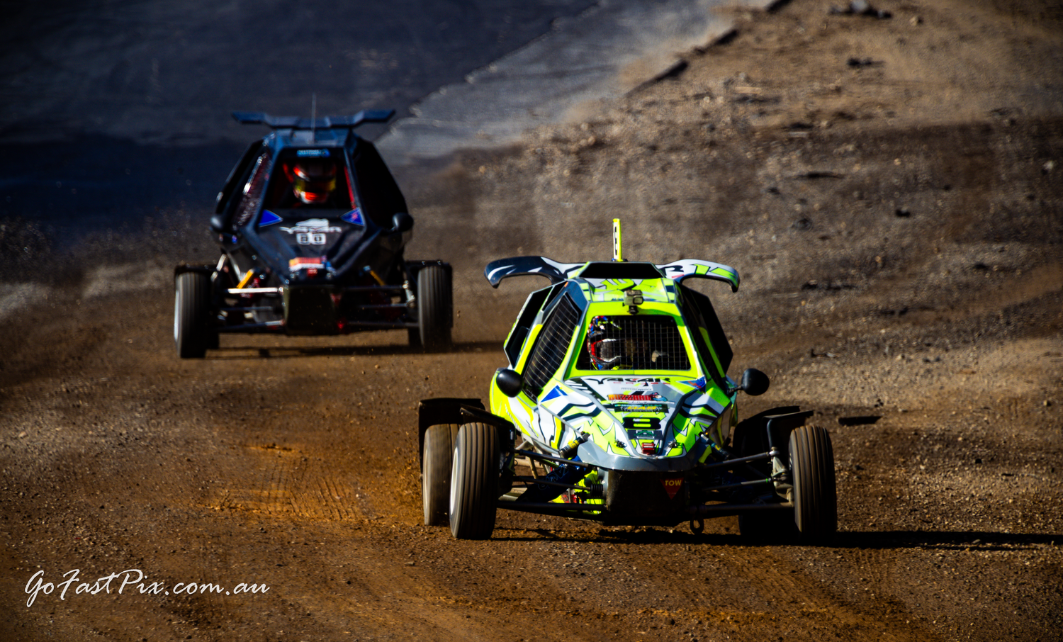 Two open-wheel off-road buggy race cars competing on a dirt racing circuit.