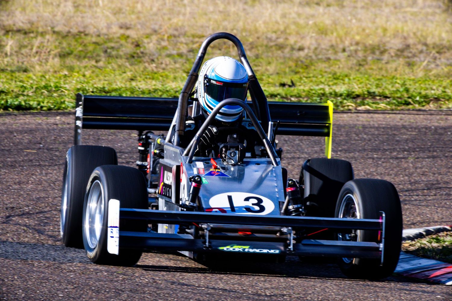 Dark blue formula-style race car number 13 driving on black asphalt racing circuit.