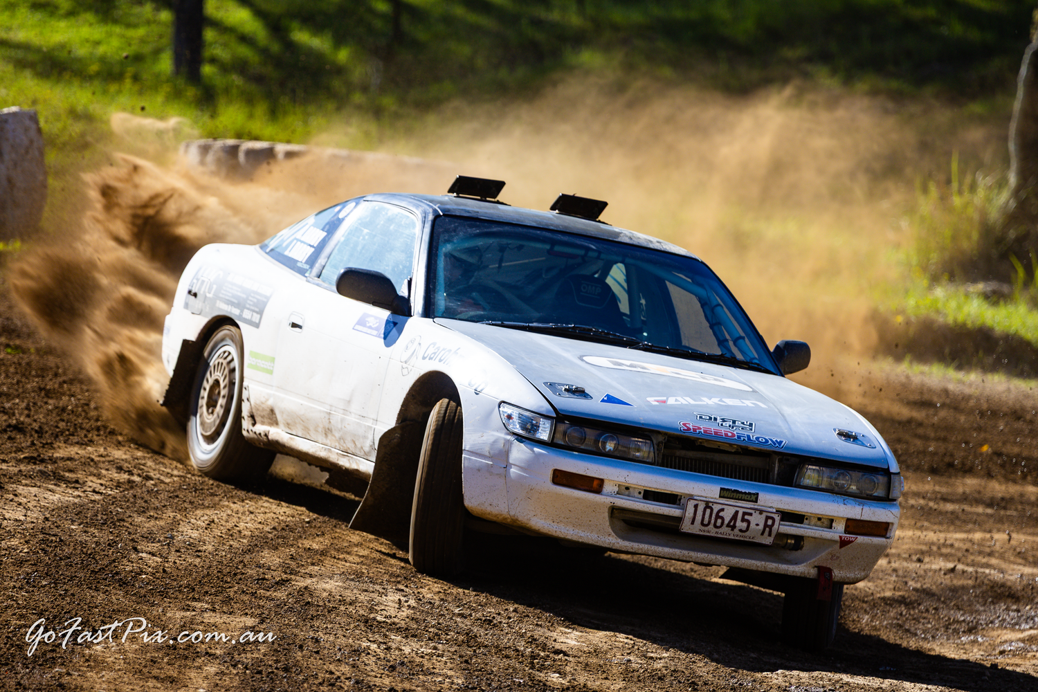 White Toyota rally car powersliding on a dusty dirt track during an Australian rally competition.