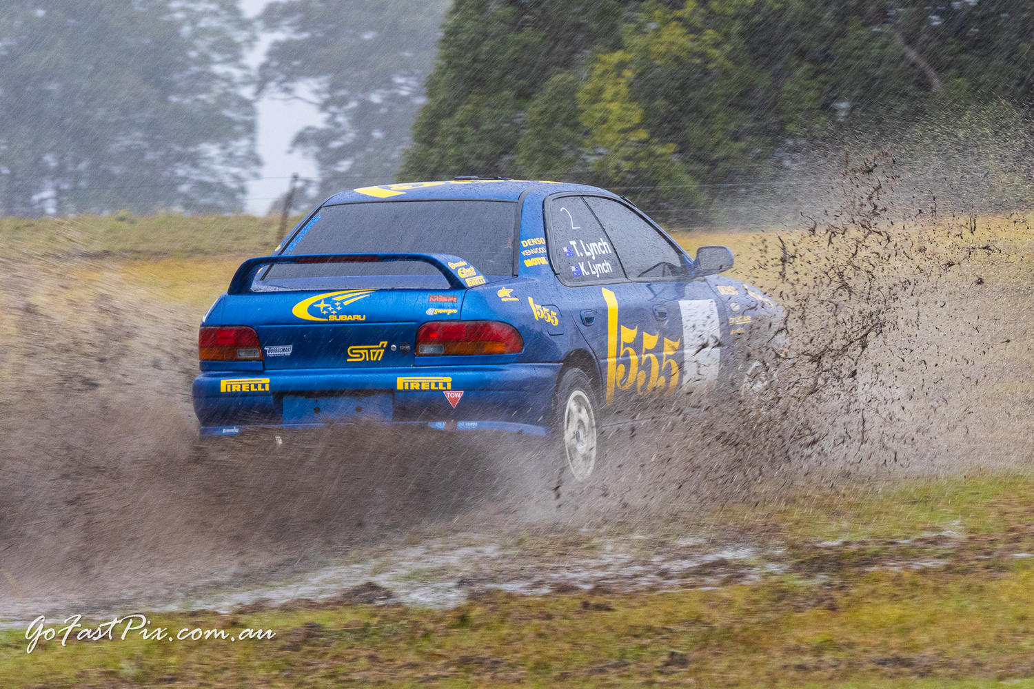 Blue Subaru Impreza WRC rally car number 555 slides through mud on stage.