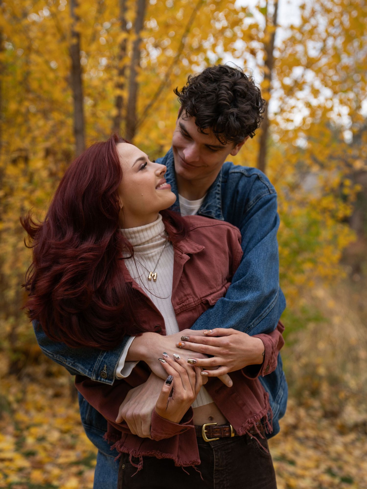 A man lifts his partner as she laughs joyfully, surrounded by bright yellow autumn leaves during an outdoor couples photo session.