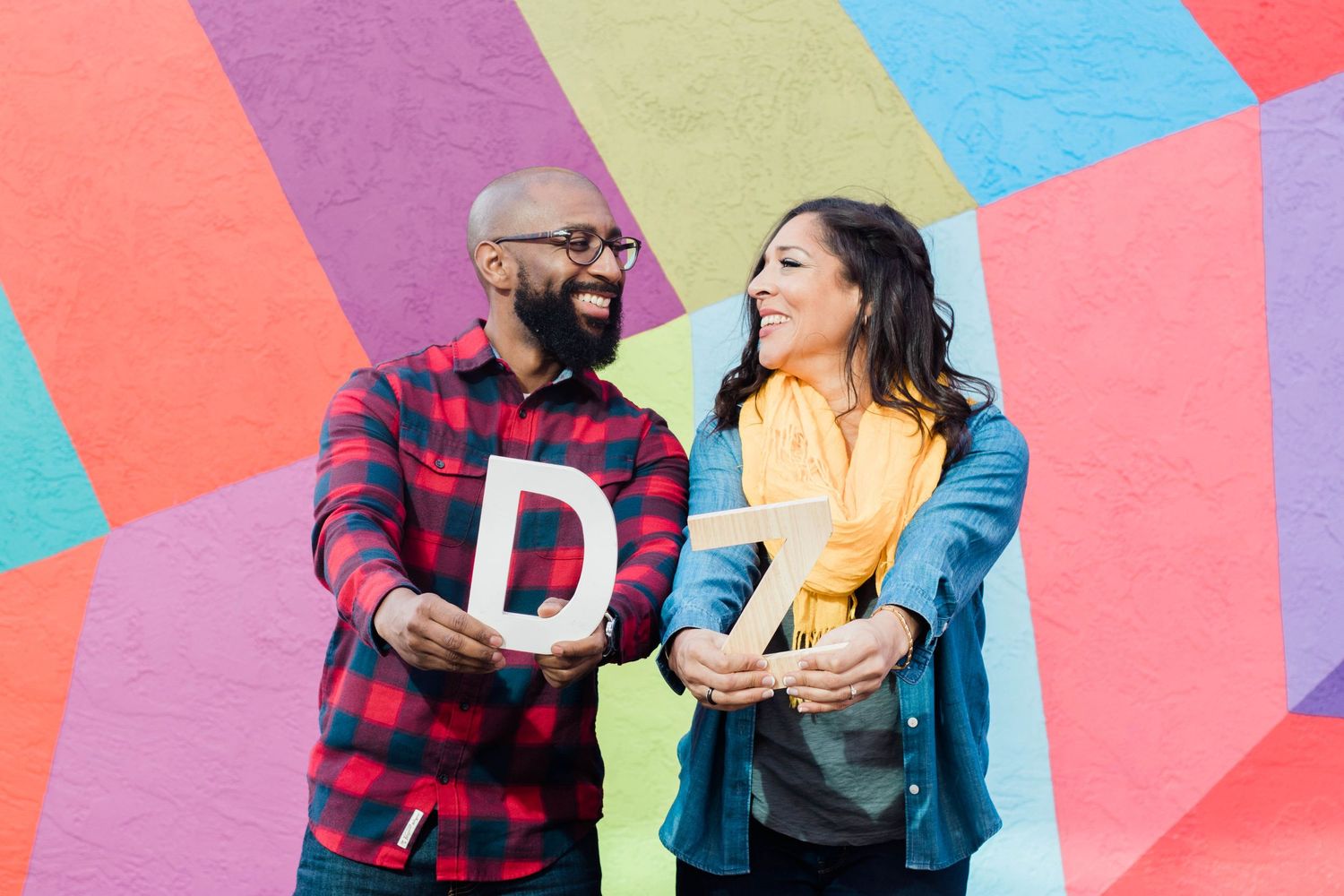 A joyful couple laughs together in front of a colorful geometric mural.