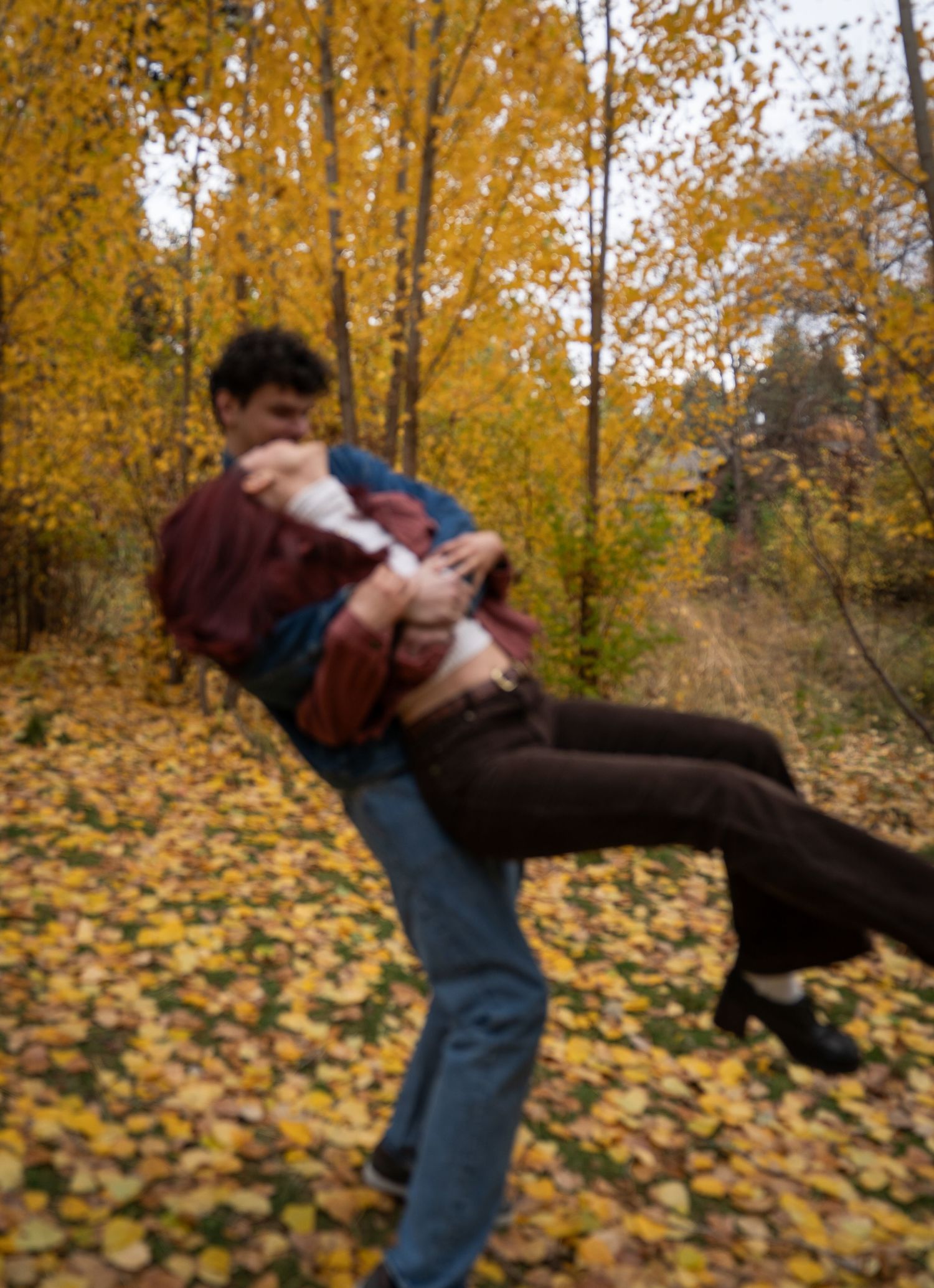 A man dips his partner dramatically among golden fall trees, both laughing during a playful outdoor couples photo session.