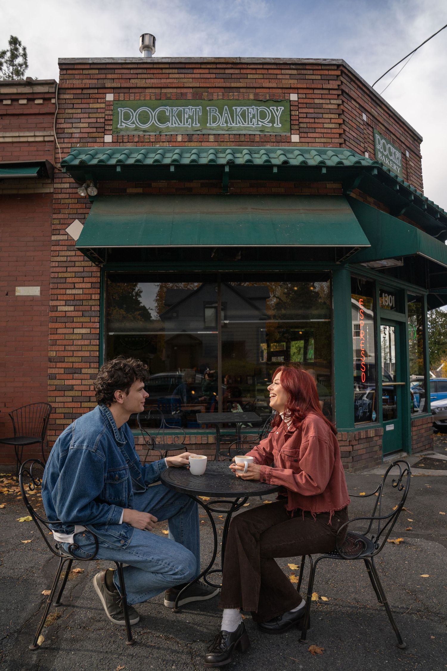 A couple sits across from each other at an outdoor café table, sharing a relaxed and candid moment during their couples photo session.