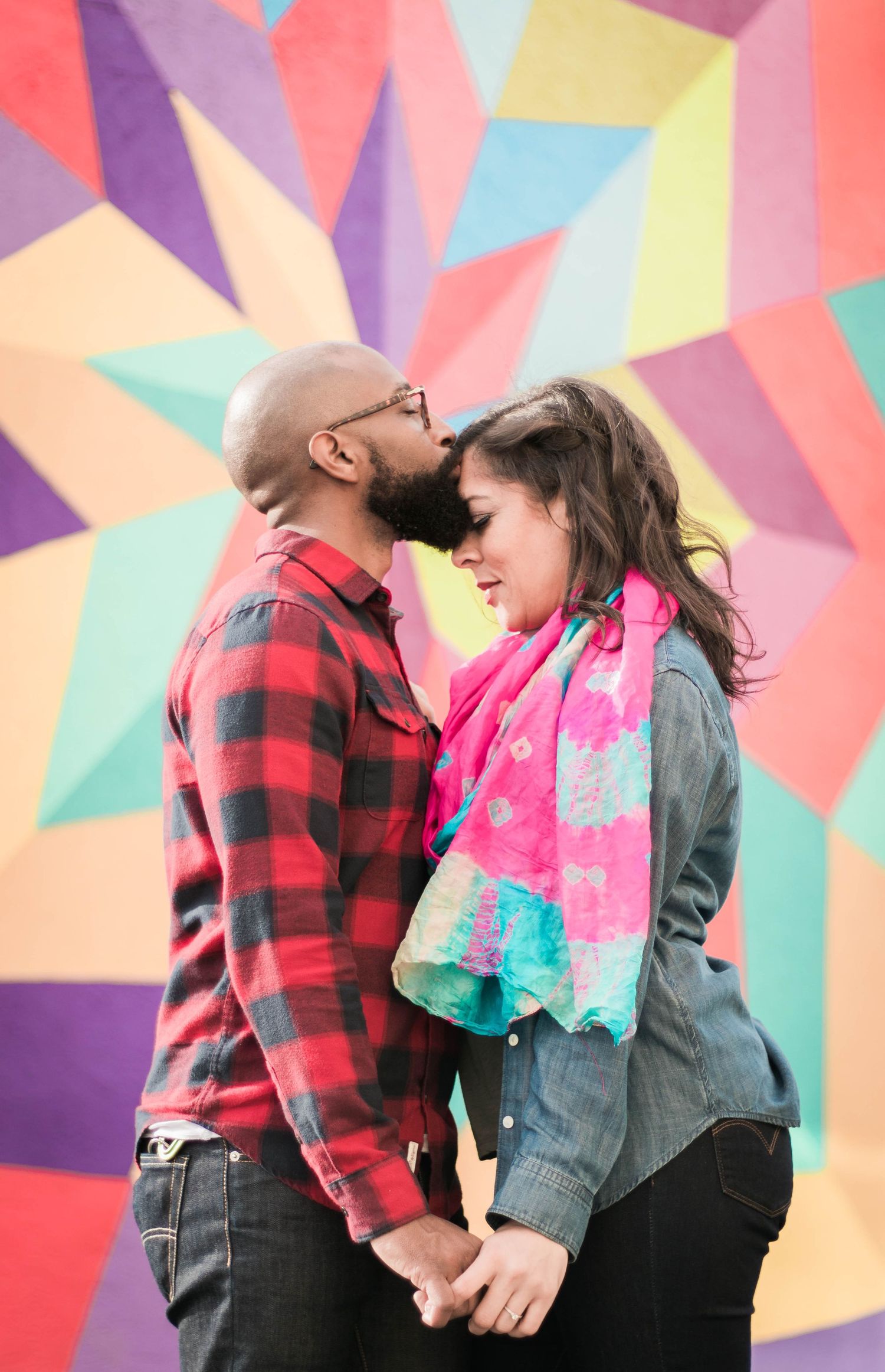 A couple shares a quiet, intimate moment nose-to-nose in front of a colorful geometric mural during an engagement session.