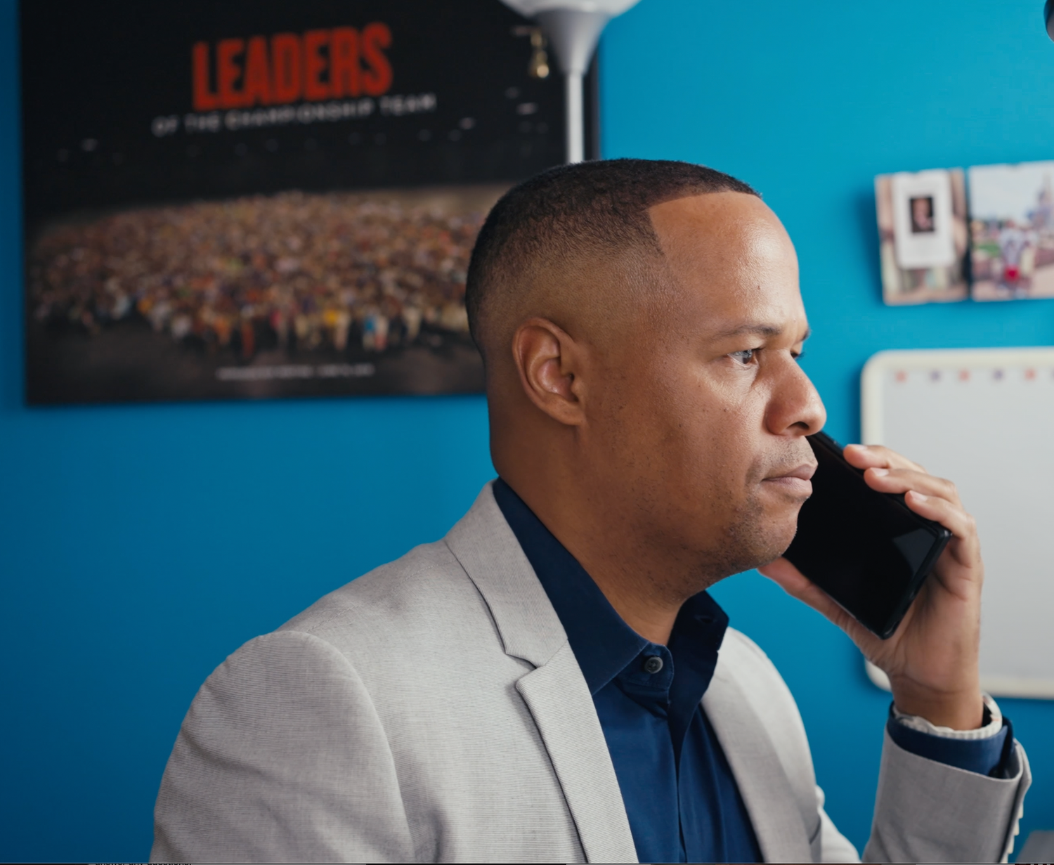 Man in gray blazer speaking on phone in a professional office setting