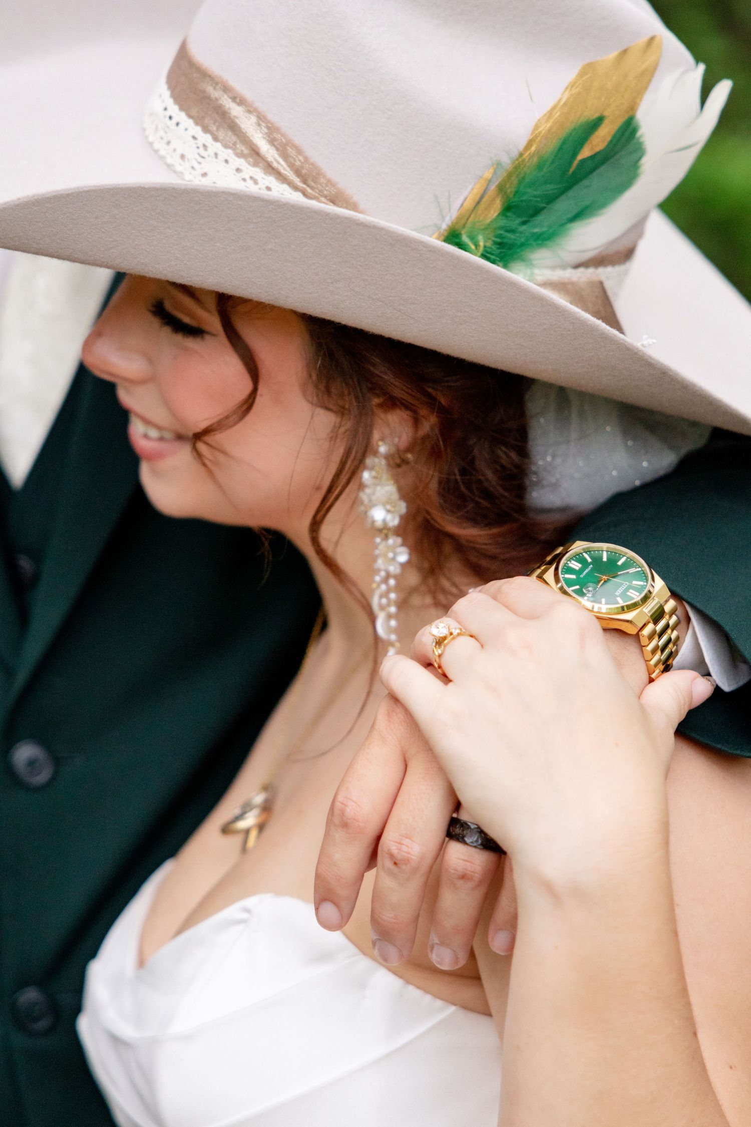 Groom in green suit with gold watch touching bride's shoulder as she wears feathered cowboy hat. Granbury Texas