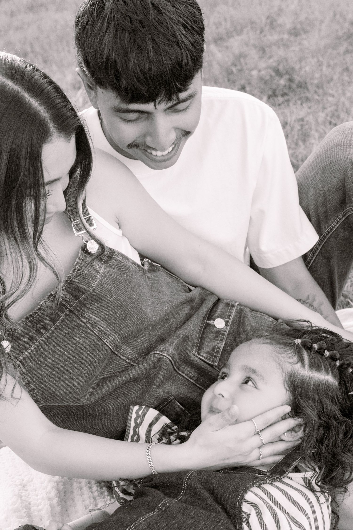 Two teens smile at young girl sitting in grass in black and white family portrait. Stephenville Texas