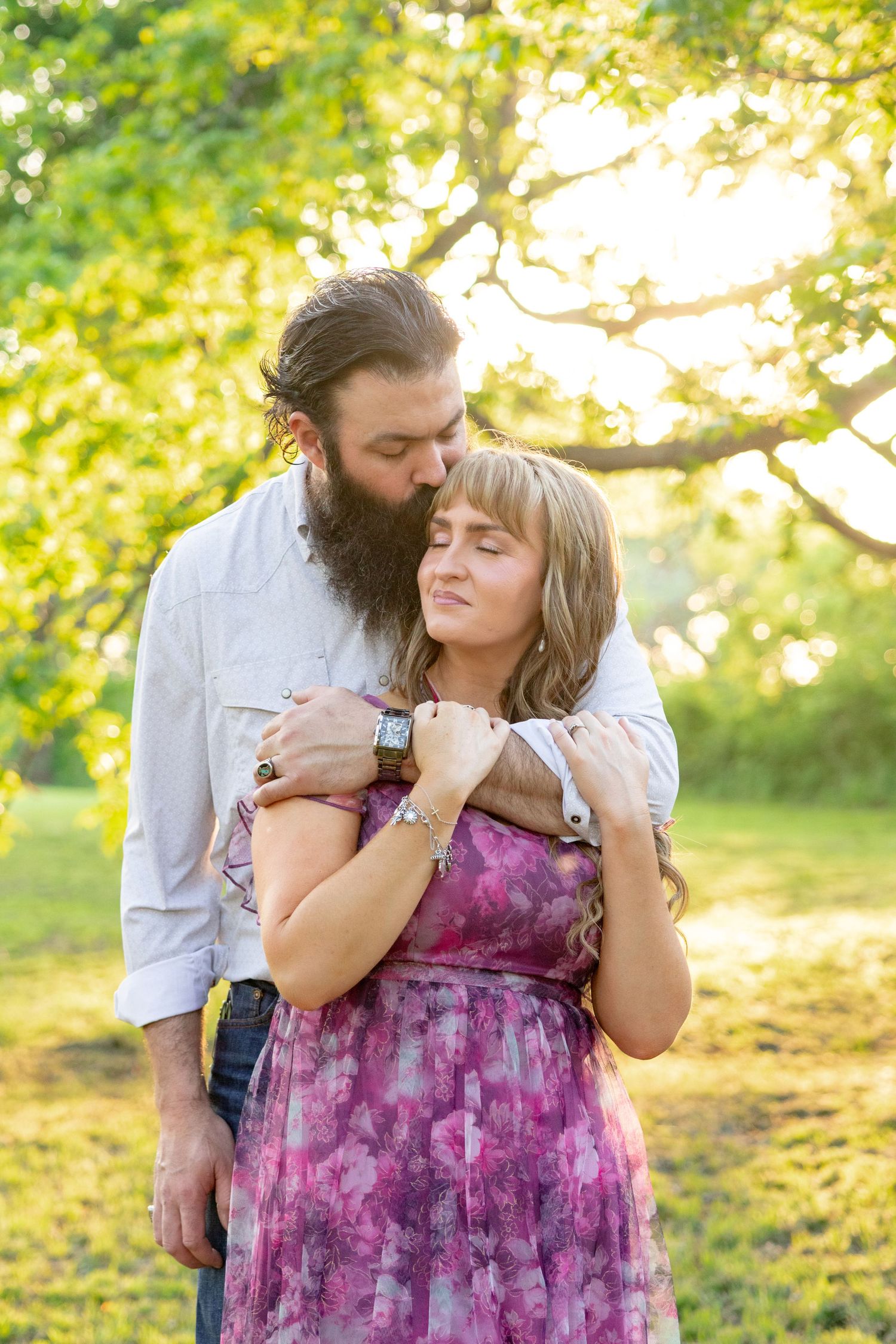 Bearded man kisses woman's head while embracing her in golden sunlit park setting. Stephenville Texas
