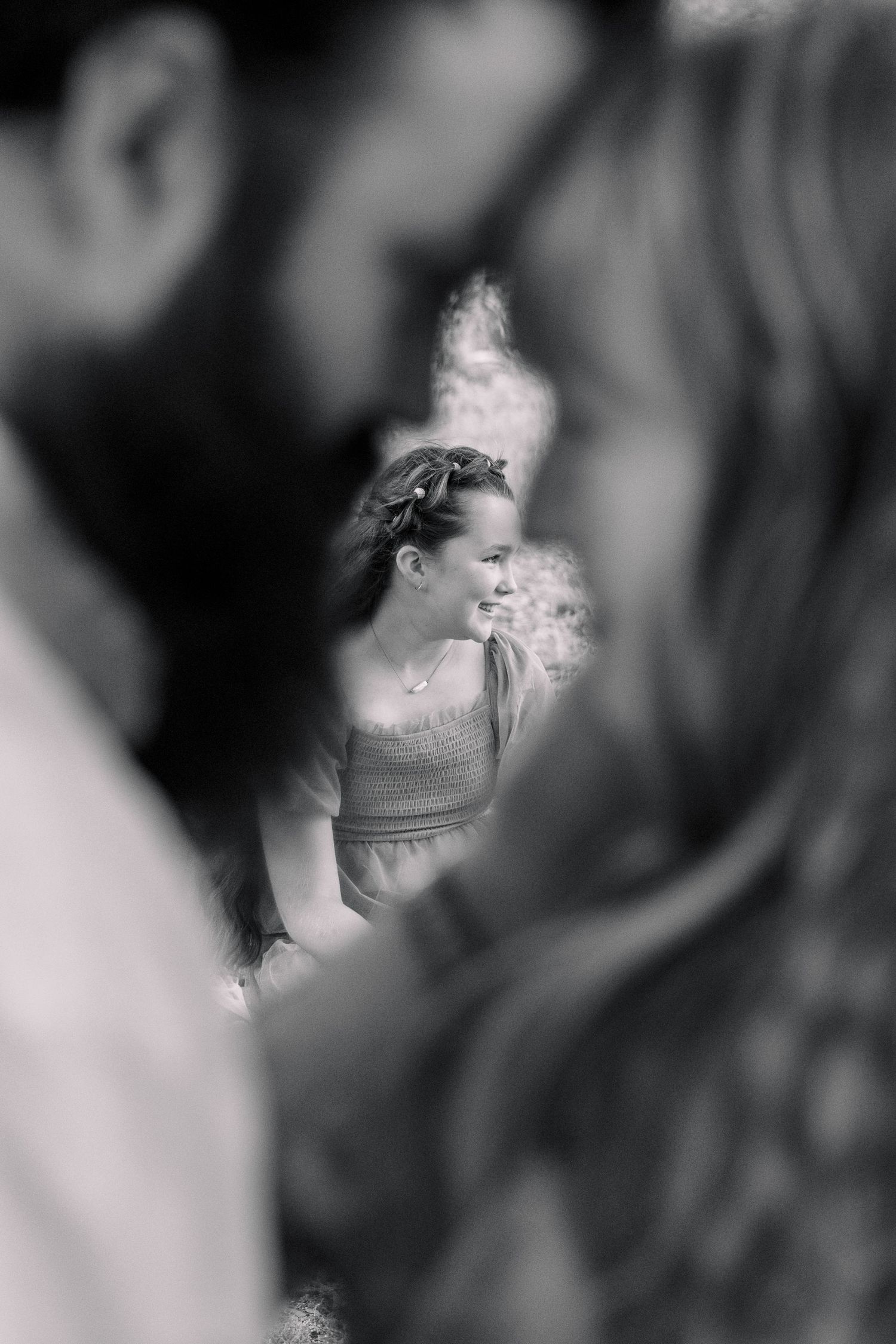 Black and white photo of a smiling woman with braided hair seen between two blurred figures in the foreground. Stephenville TX Photographer