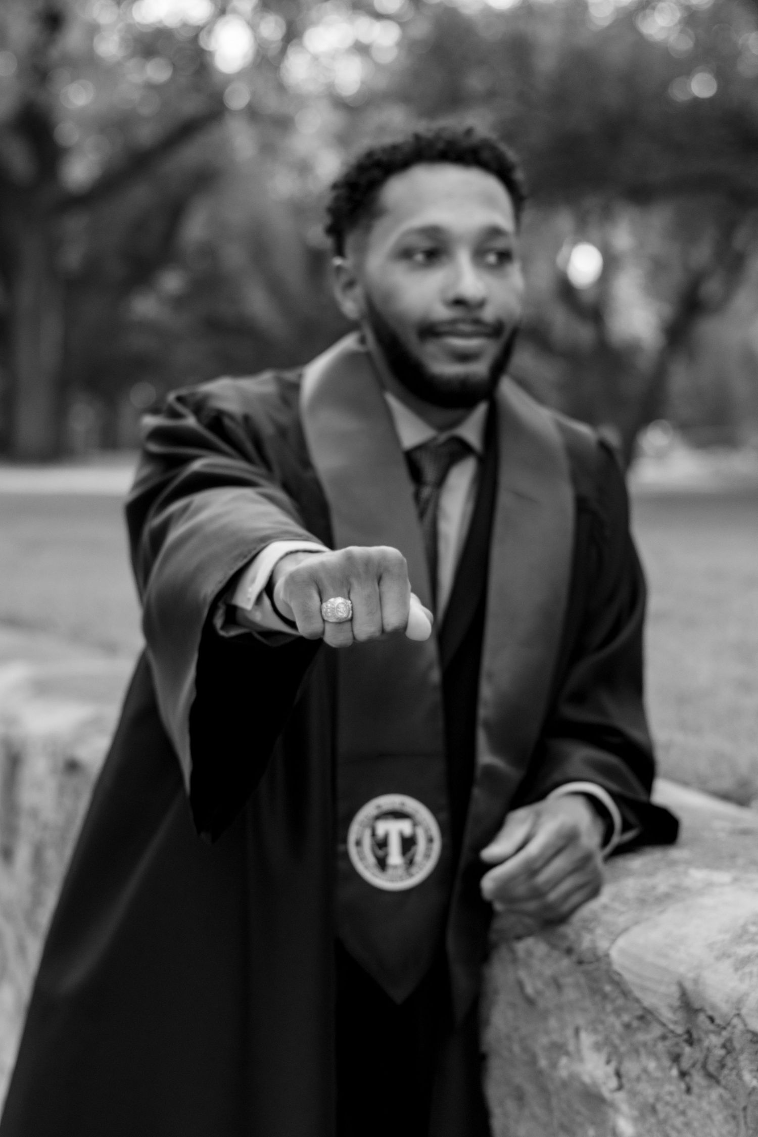 Black and white graduation photo of a young man in academic regalia extending a ring toward the camera outdoors. TARLETON STATE UNIVERSITY