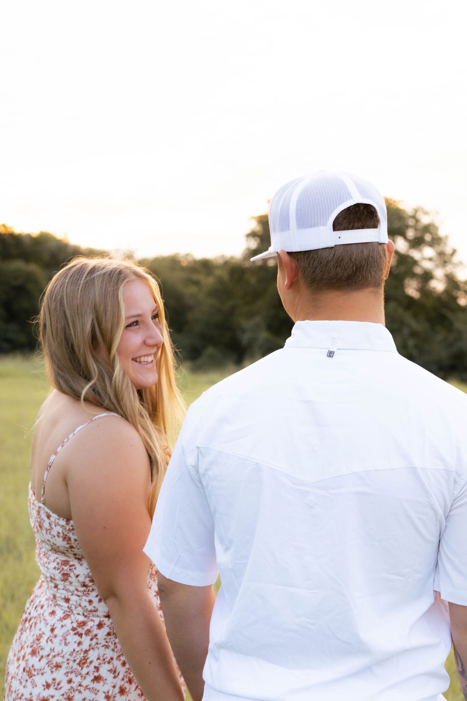 Smiling blonde woman in floral dress holding hands with partner at sunset.