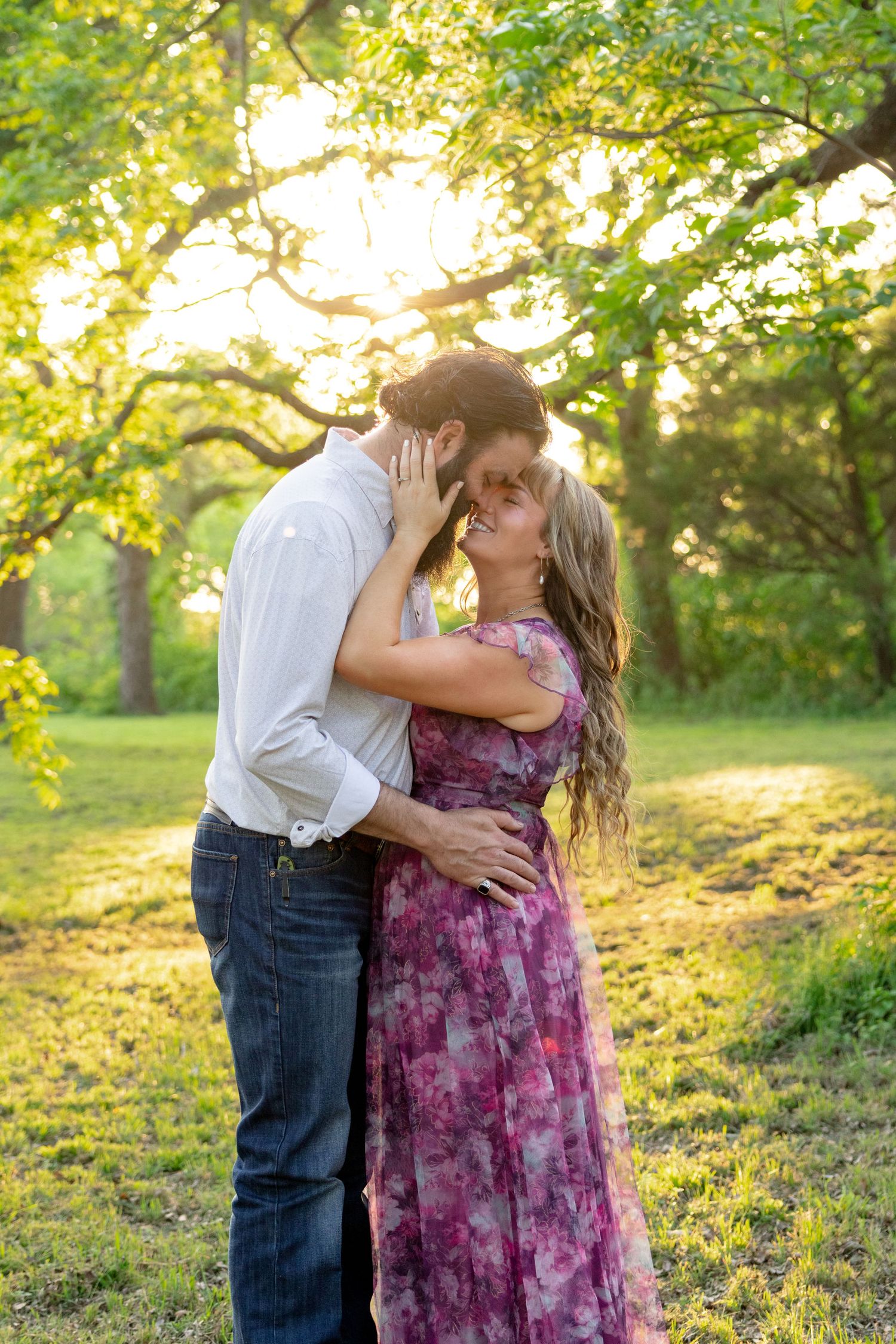Couple sharing a kiss in a sunlit park, woman in pink floral dress, golden hour lighting. Stephenville Texas