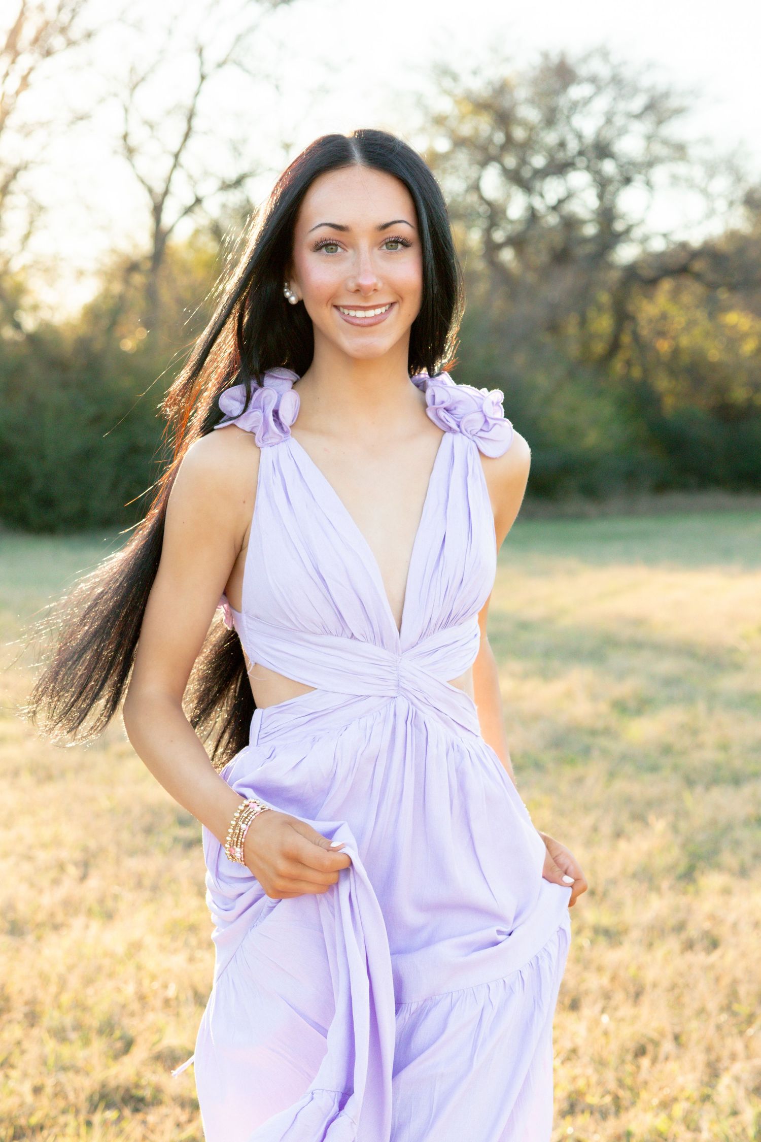 Smiling woman in lavender dress poses in sunlit field with flowing dark hair. Stephenville Texas Photographer