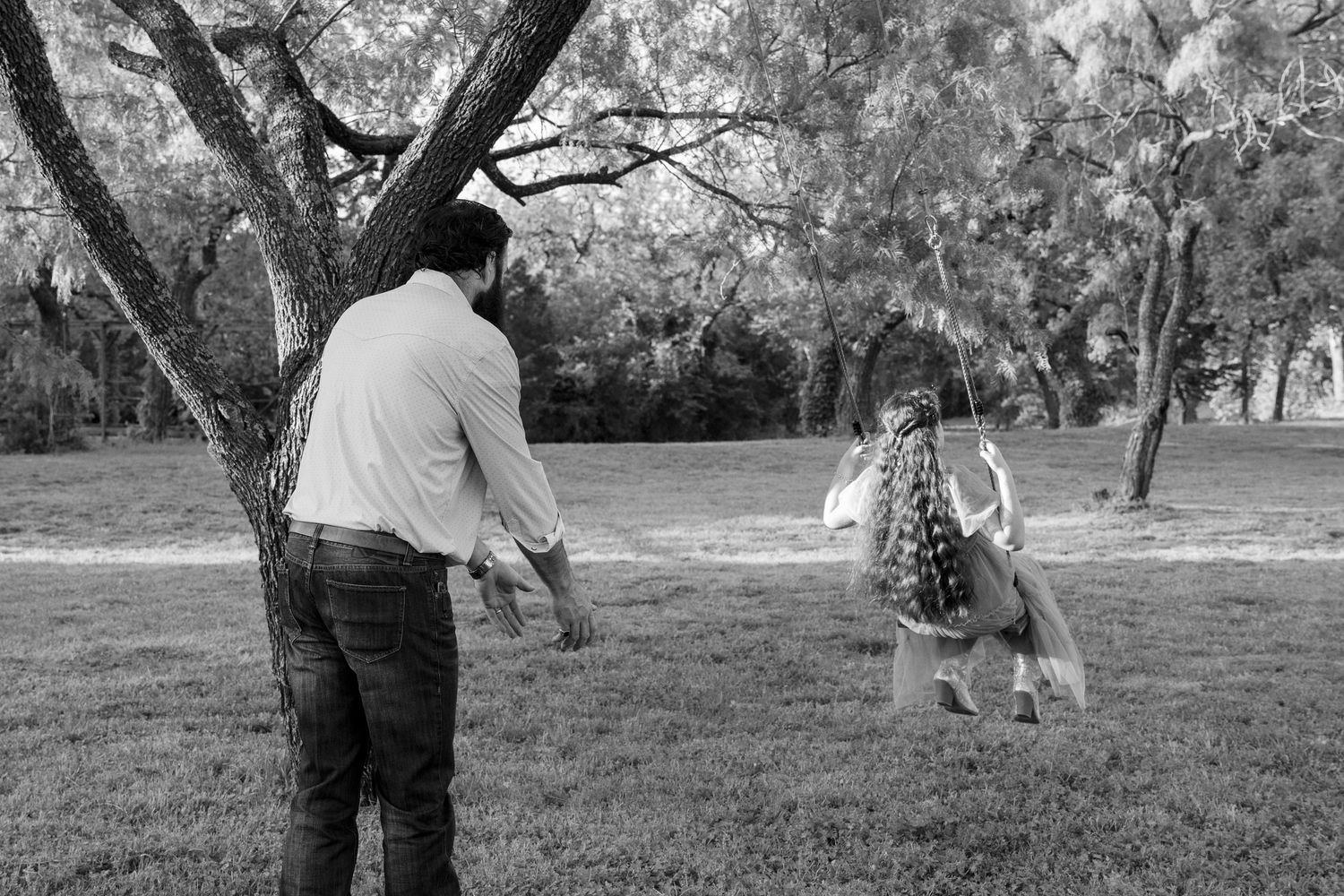 Black and white photo of a father and child playing outdoors near a tree in a park. Stephenville TX Photographer