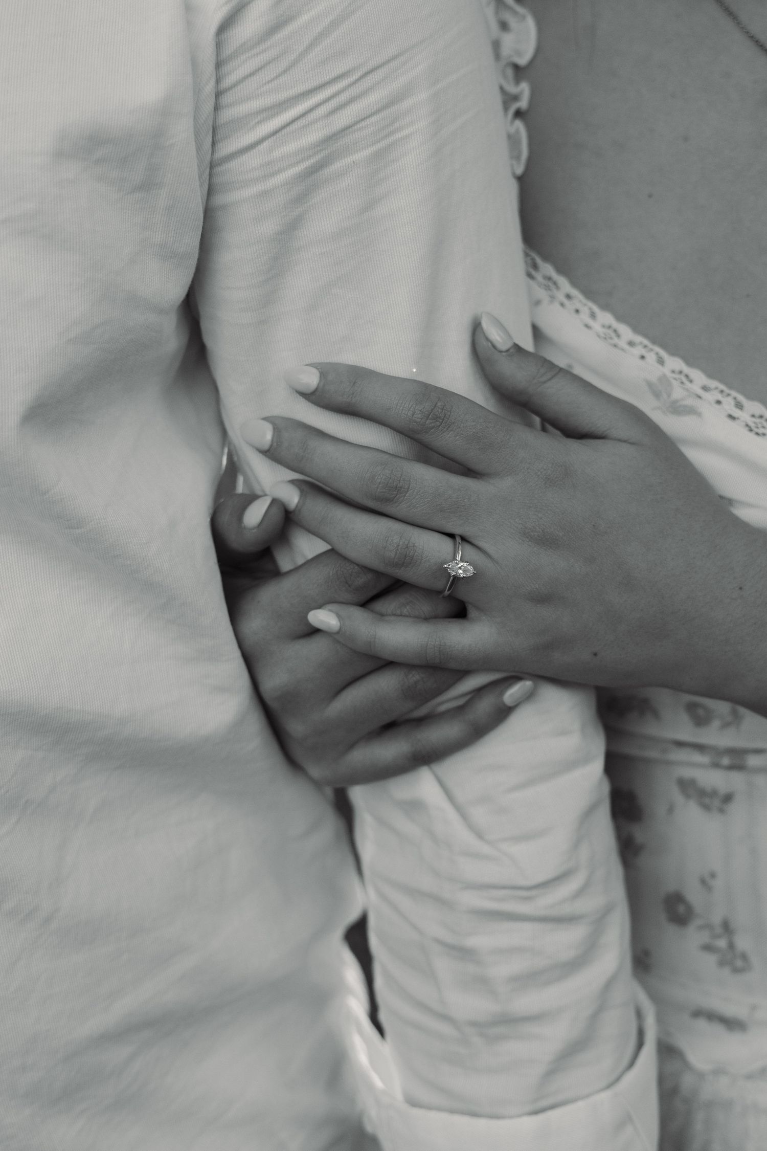 Close-up black and white photo of couple embracing, woman's hand showing a diamond engagement ring wrapped around man's waist. San Antonio