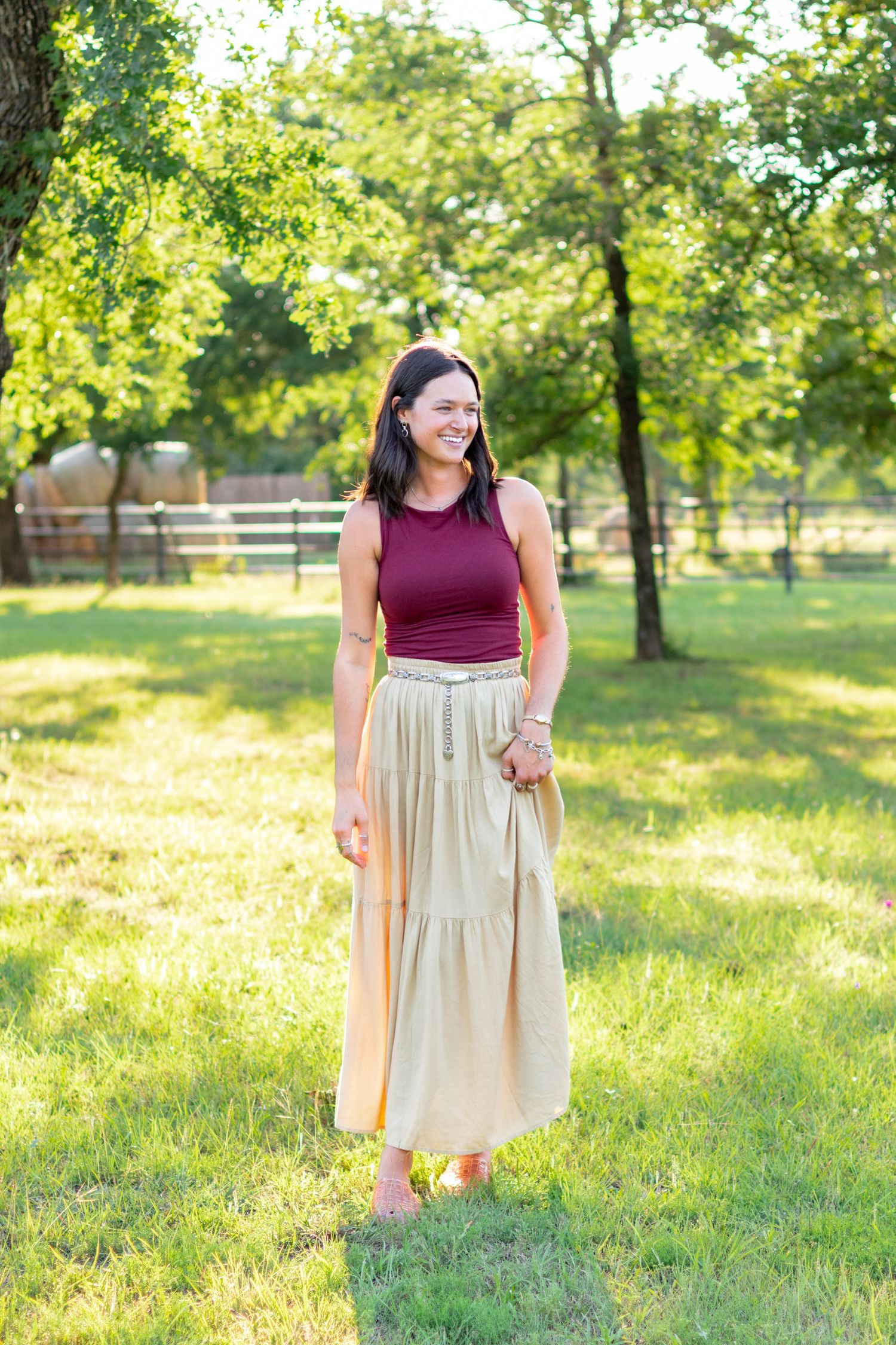 Smiling brunette woman in burgundy tank and gold tiered maxi skirt walking outdoors. Stephenville texas