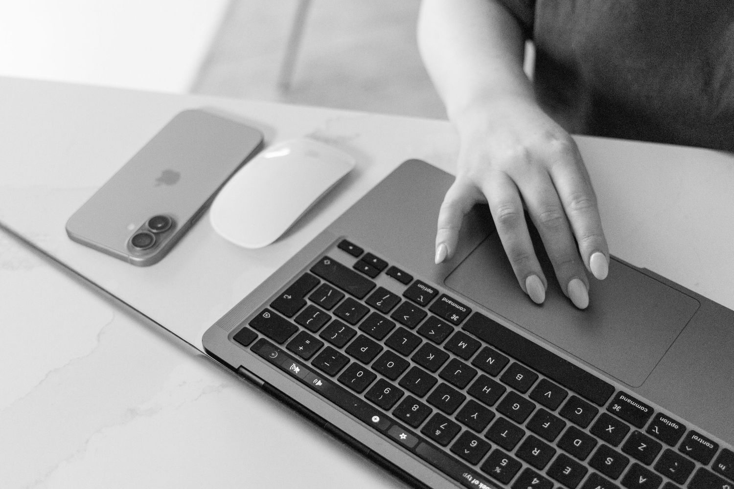 Black and white photo of a woman using a MacBook laptop beside an iPhone and Apple Magic Mouse on a desk.
Emma - Reefolution - Brandingshoot