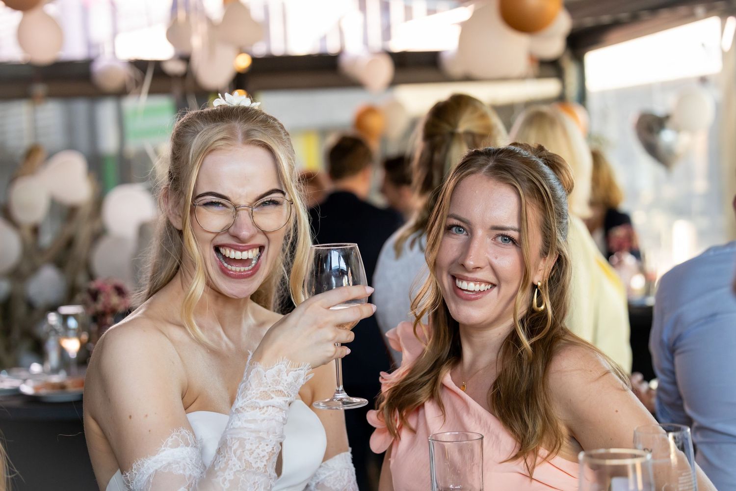 Two smiling women toasting with champagne glasses at an elegant wedding reception celebration.