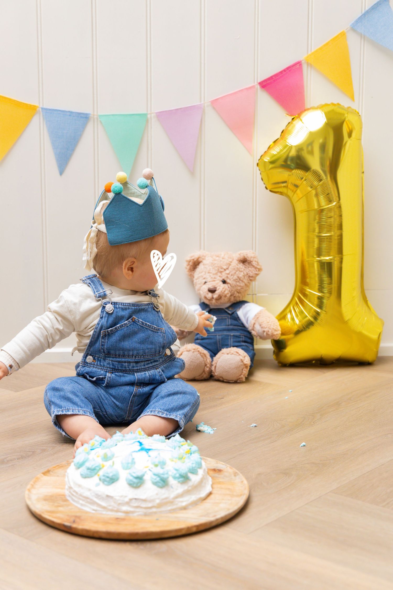 Baby's first birthday cake smash with teddy bear, gold number 1 balloon, and colorful bunting decorations.