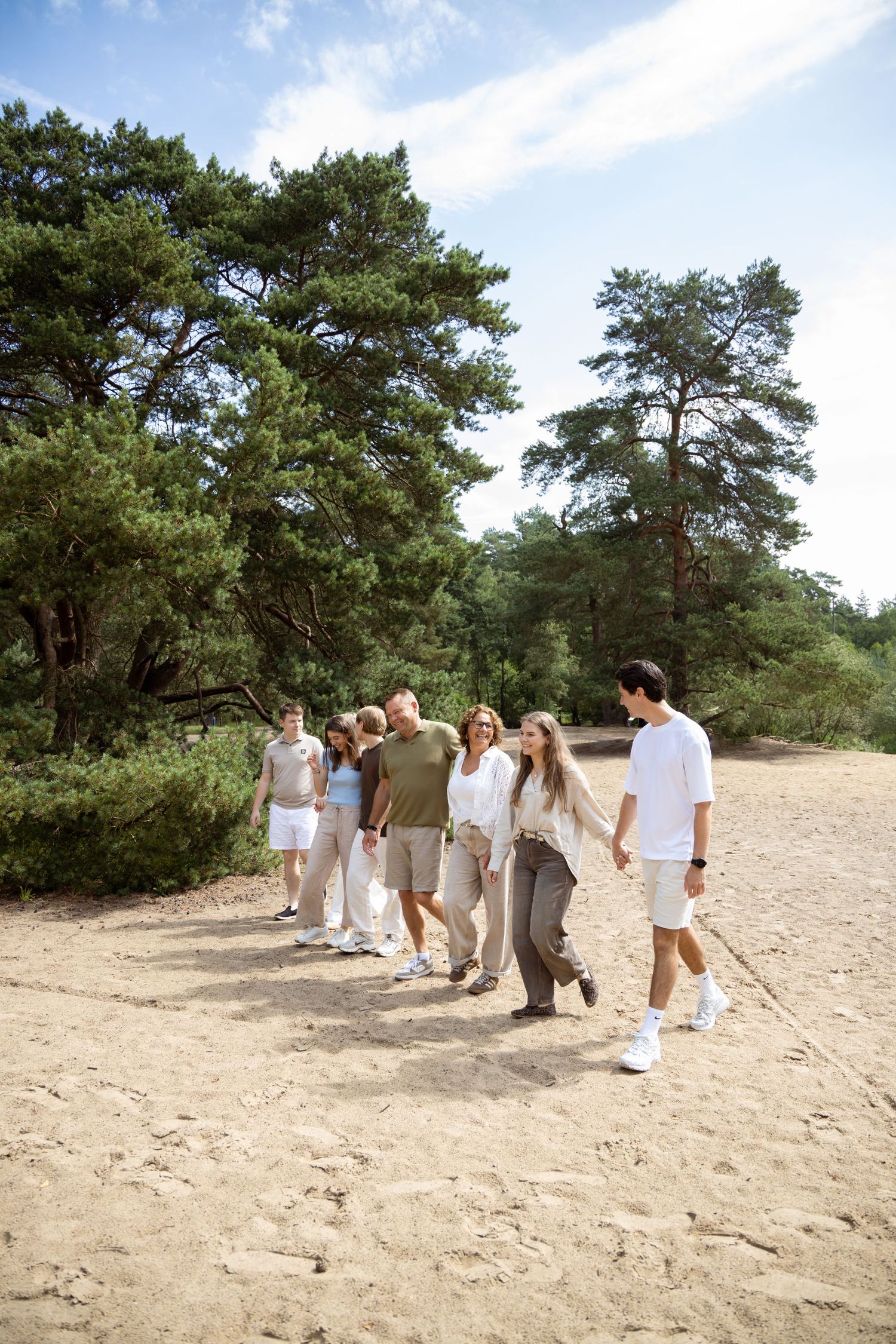 Family walking together on sandy path surrounded by tall green pine trees on a sunny day.
Familie Wormgoor - Familieshoot