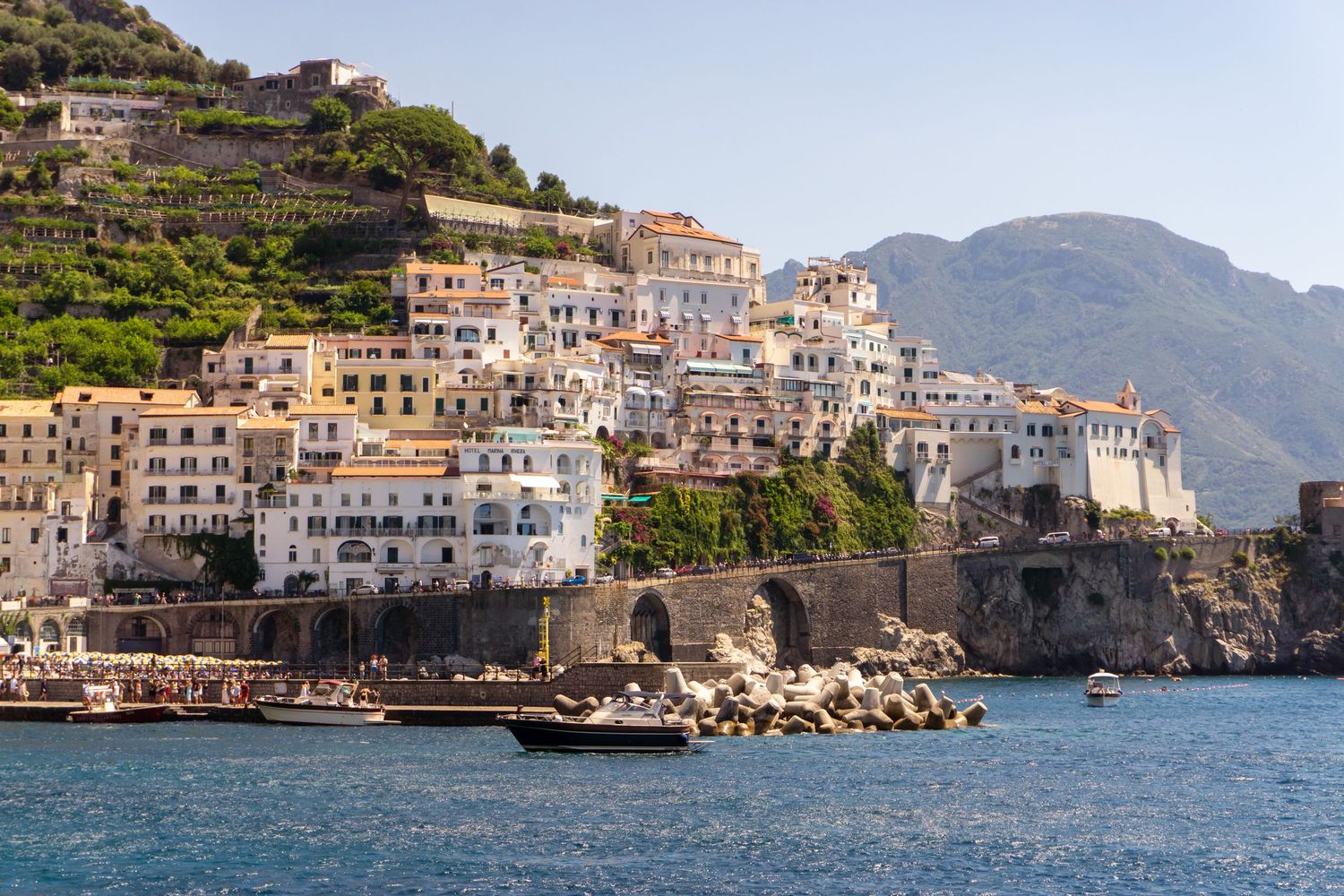 Colorful cliffside buildings of Amalfi Coast, Italy, overlooking crystal-blue Mediterranean waters with rocky shoreline.
Lynn - Amalfi